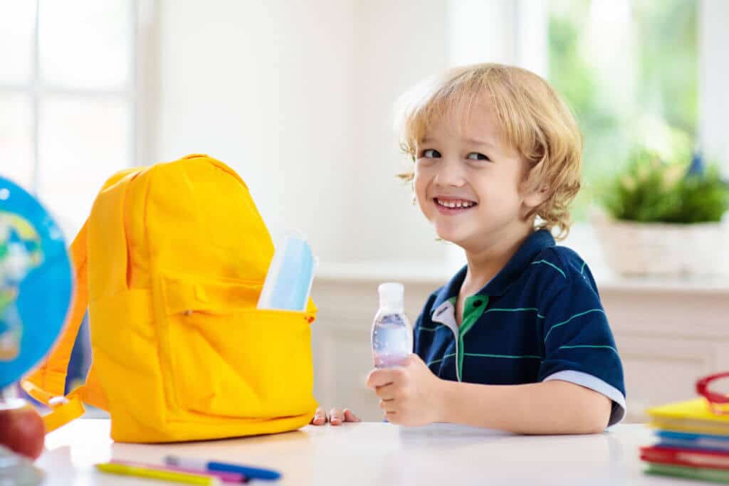 Child at a childcare center prepared for COVID-19 with hand sanitizer and a face mask.
